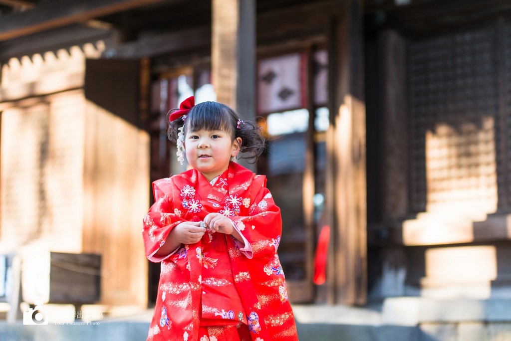 神社本殿の前で赤い着物を着て立っている女の子