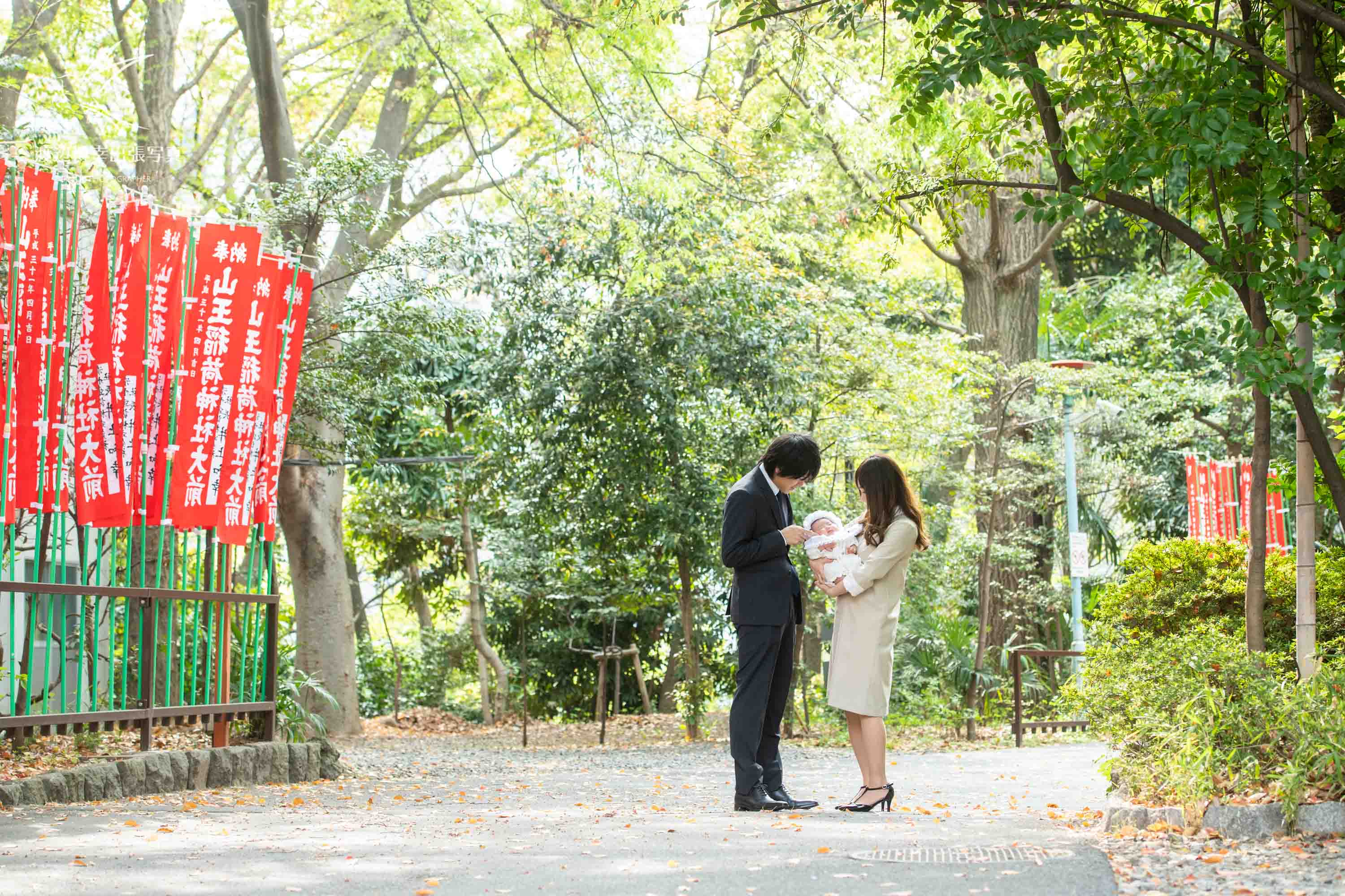 赤坂の日枝神社の千本鳥居の前でお宮参りの掛着を着て赤ちゃんを抱く夫婦の写真