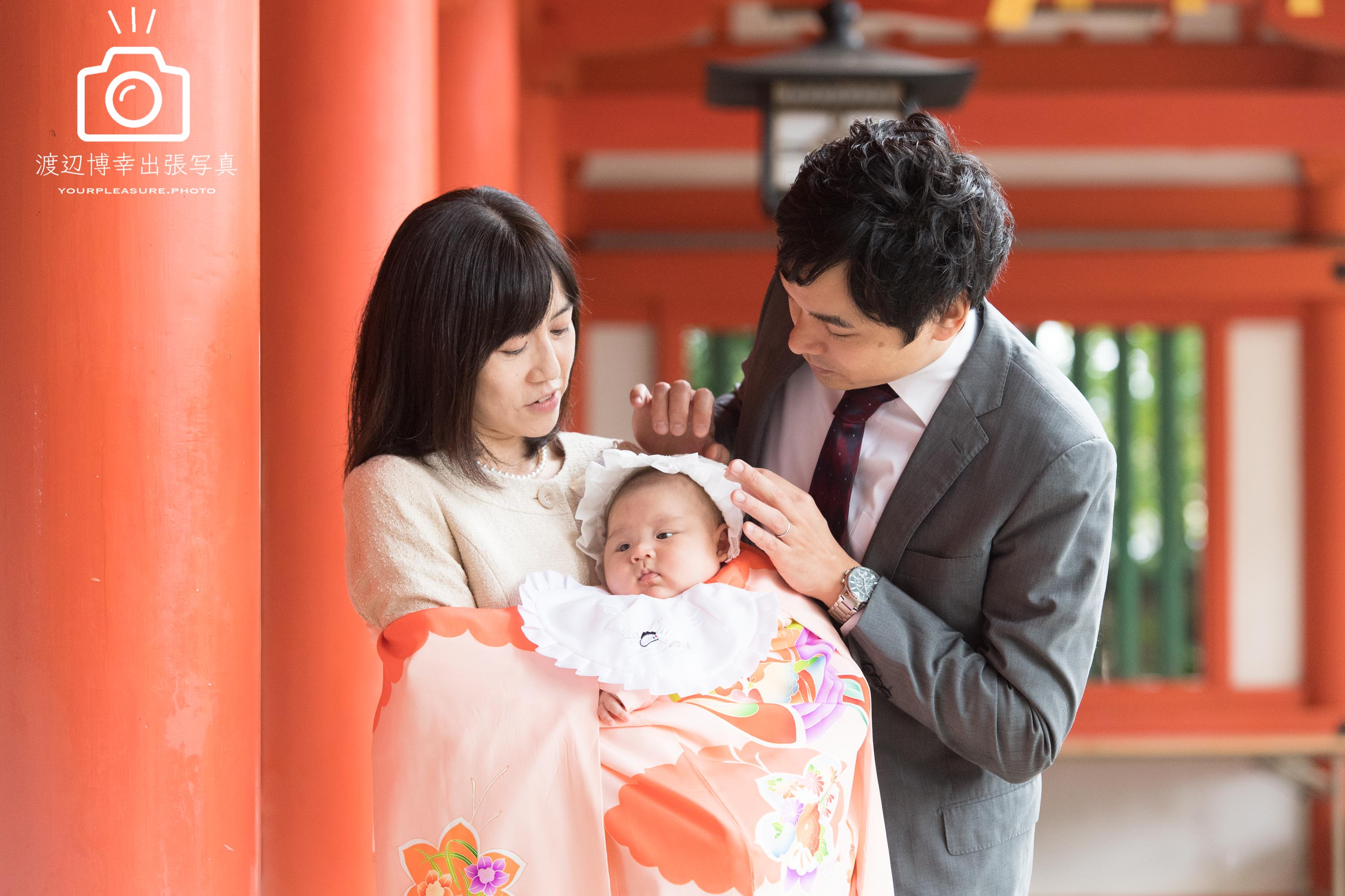 大宮氷川神社の回廊の赤い柱のそばに立つ赤ちゃんを抱っこした掛着姿のママとパパ