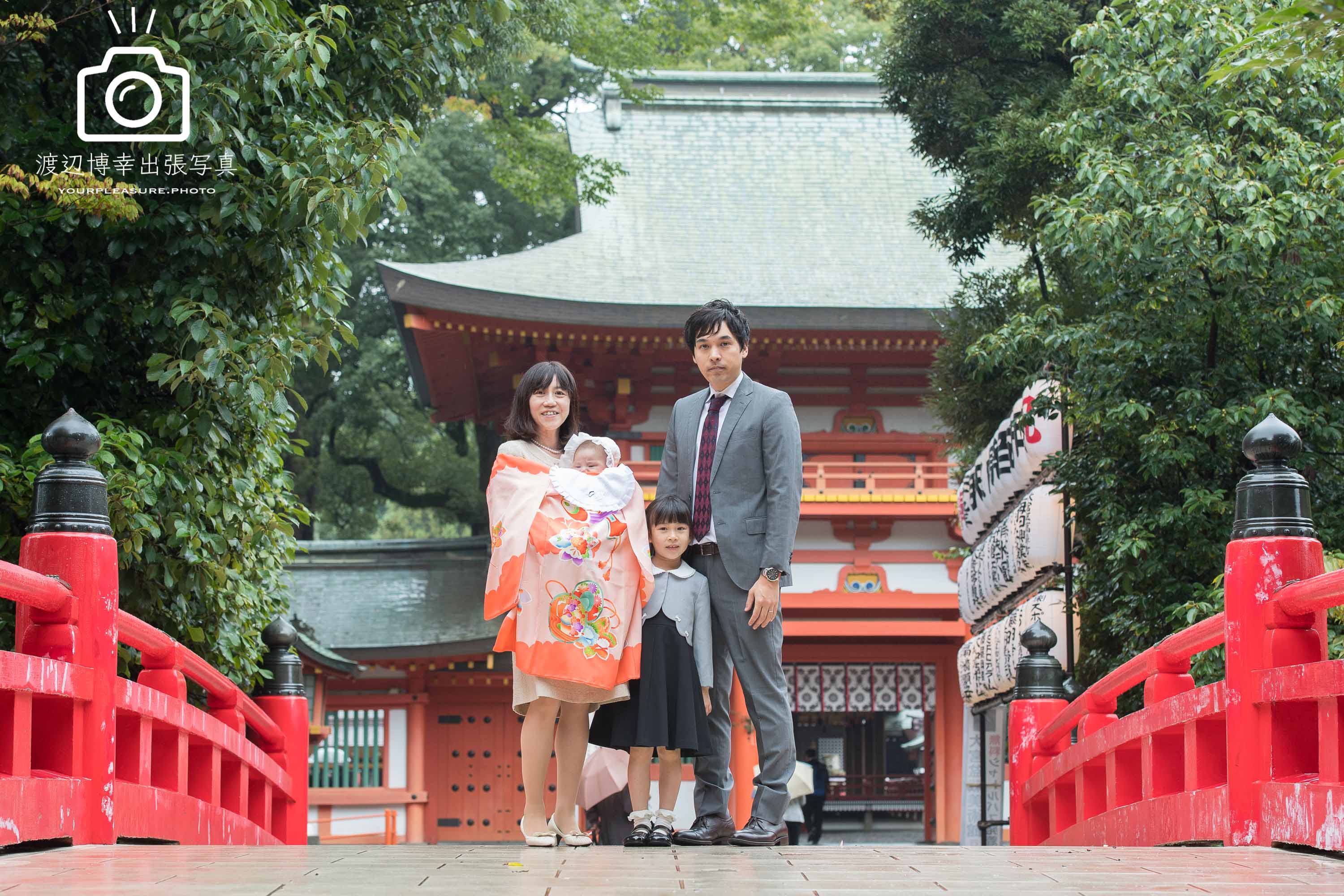 大宮氷川神社の赤い橋の上に立つお宮参りに来た家族