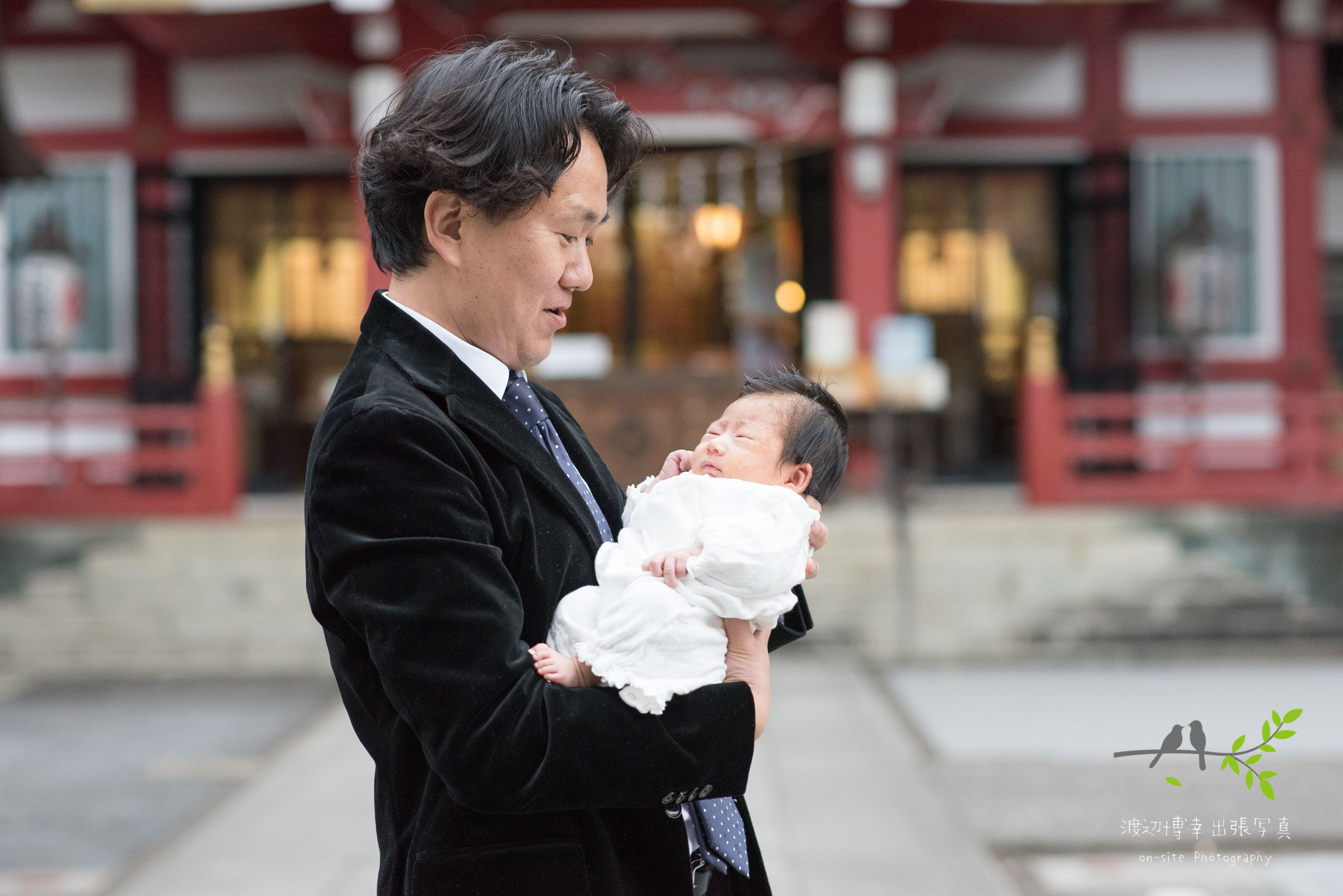 神社本殿の前で赤ちゃんを抱き立つ父親