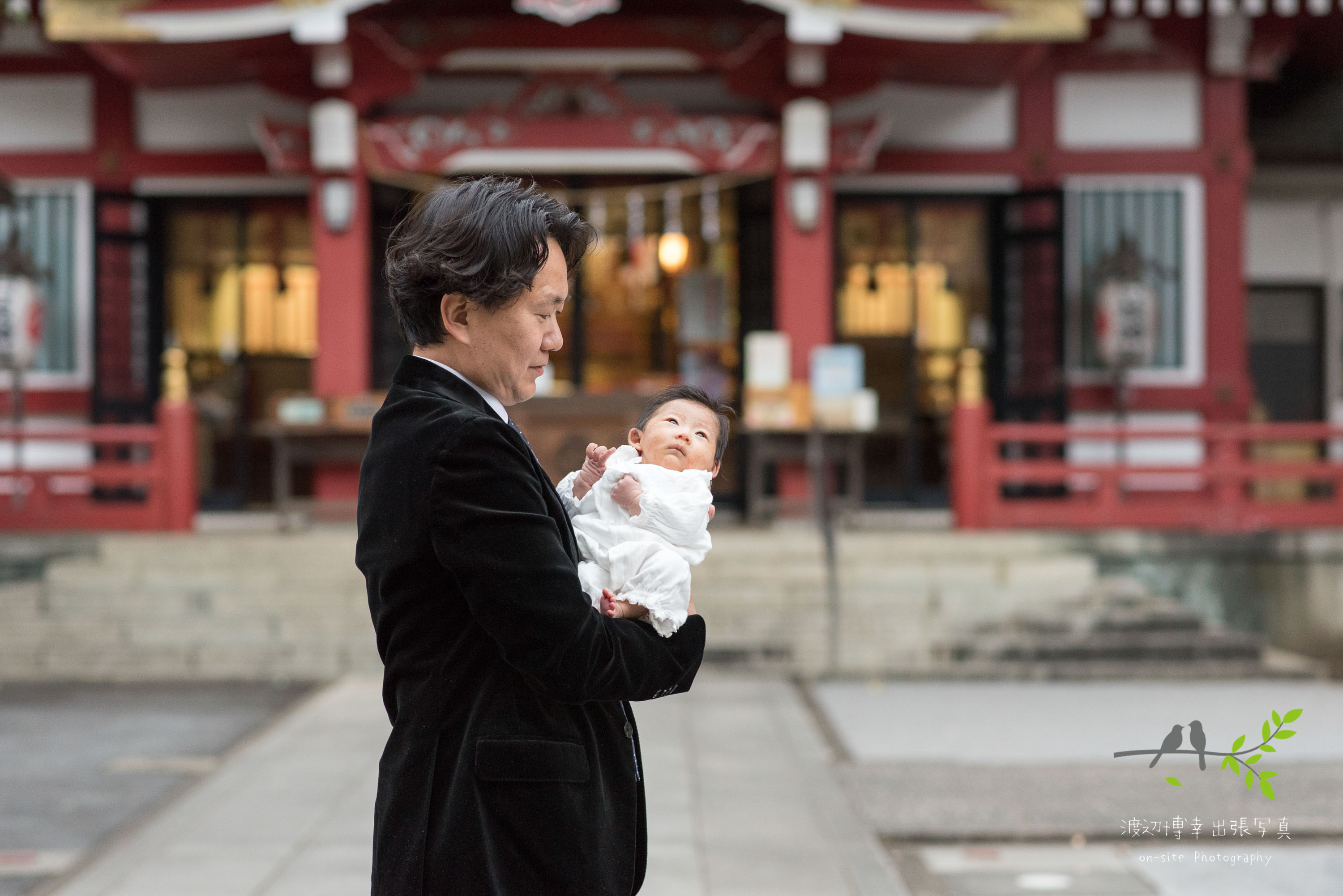 神社本殿の前で赤ちゃんを抱き立つ父親