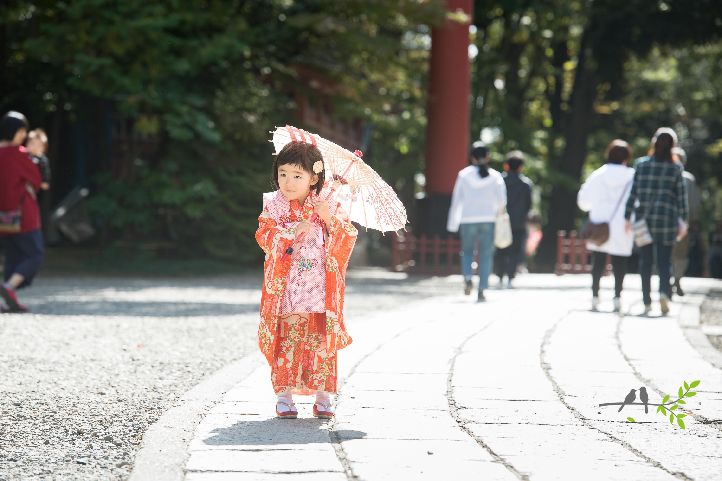和傘をさし参道を歩くオレンジ色の着物姿の小さな女の子