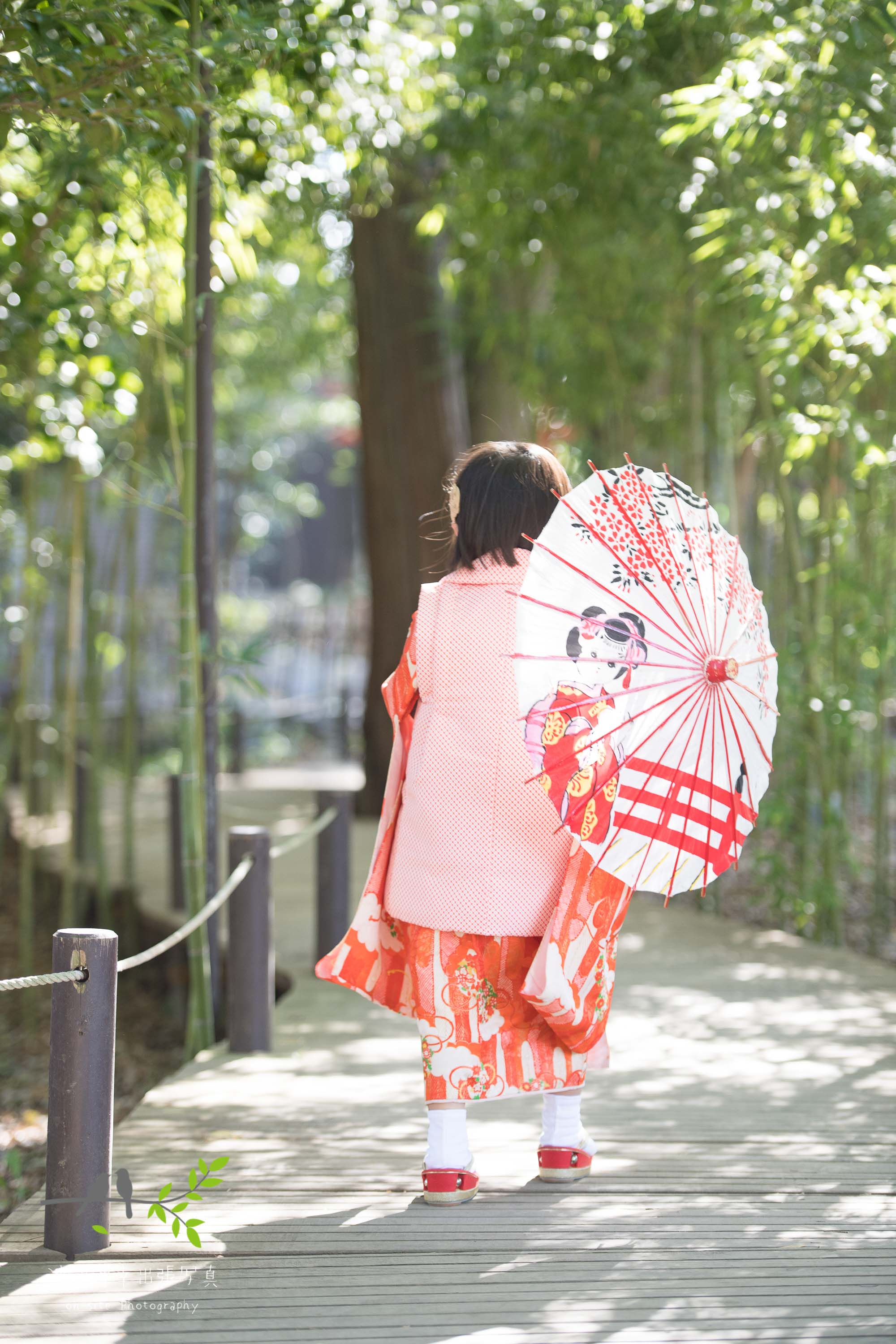 和傘をさすオレンジ色の着物姿の小さな女の子の後ろ姿