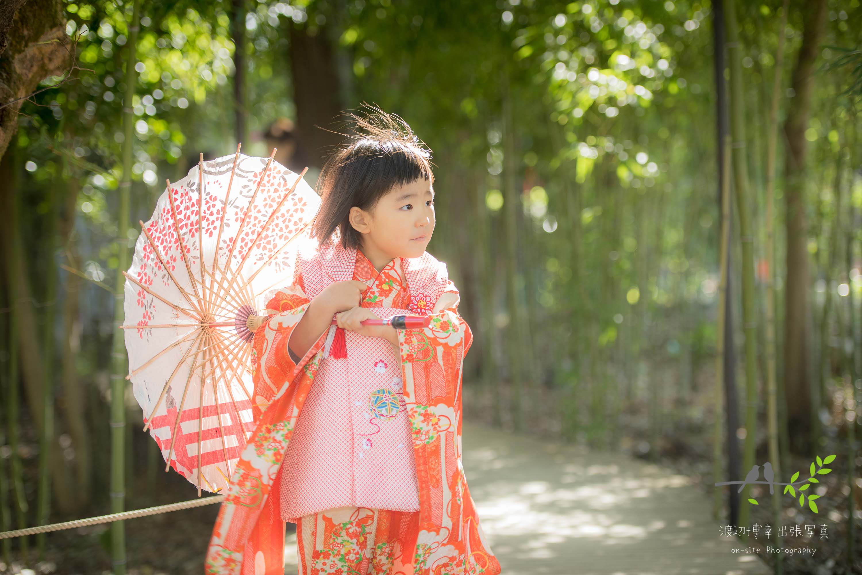 和傘をさして立つオレンジ色の着物姿の小さな女の子