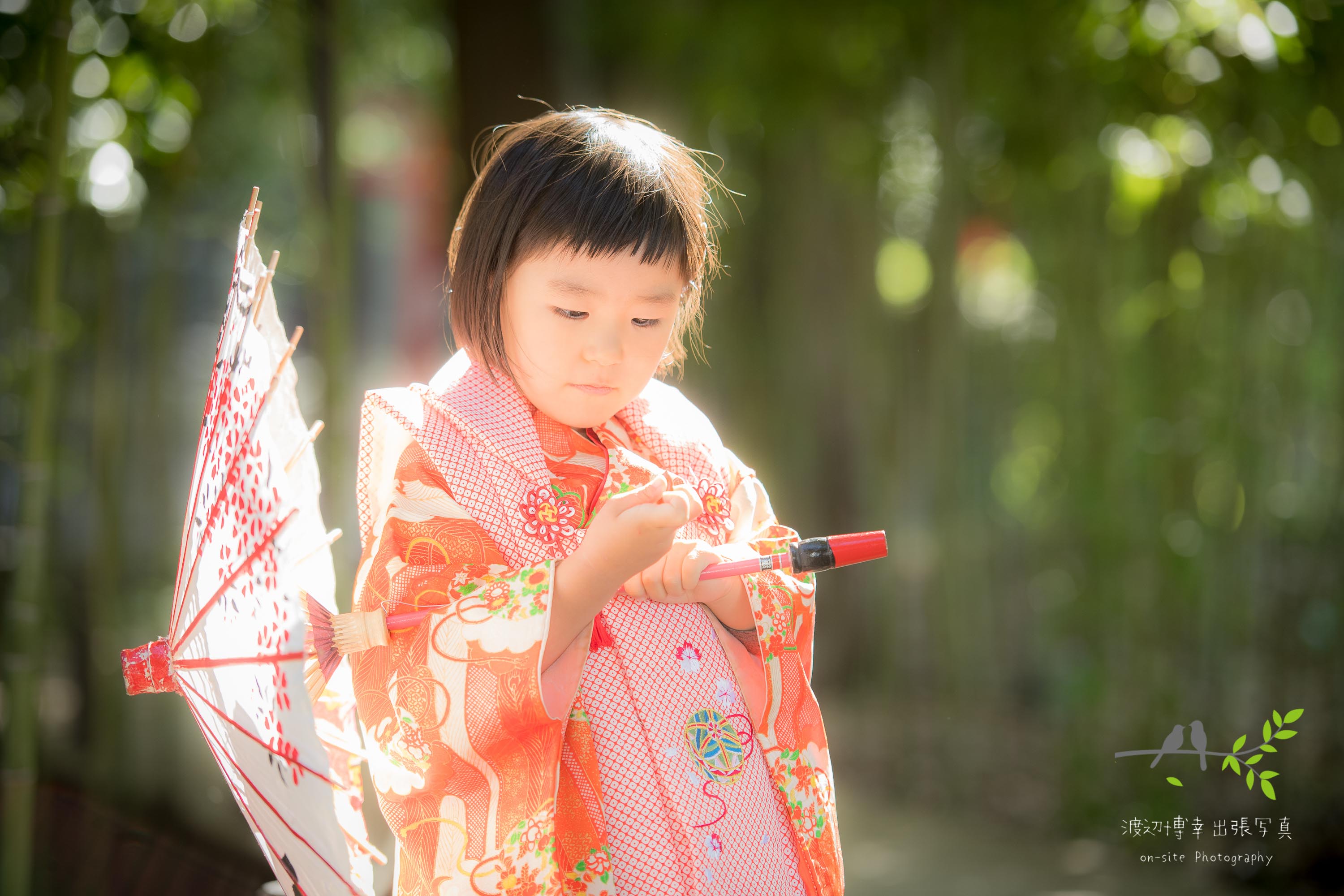 和傘をさして立つオレンジ色の着物姿の小さな女の子