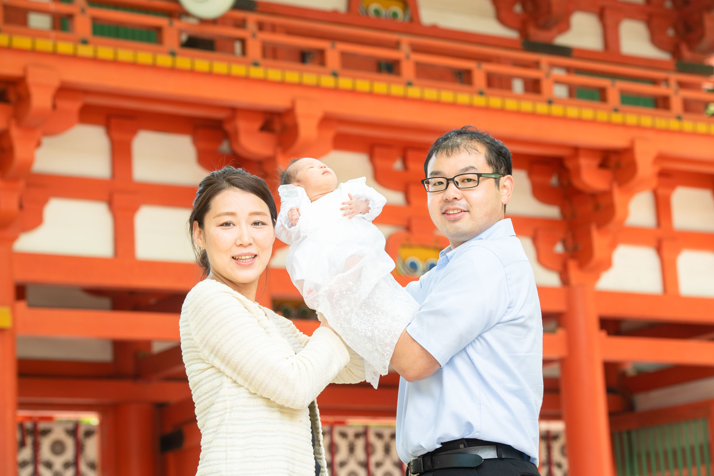 赤い神社門も前で赤ちゃんを抱く女性と男性