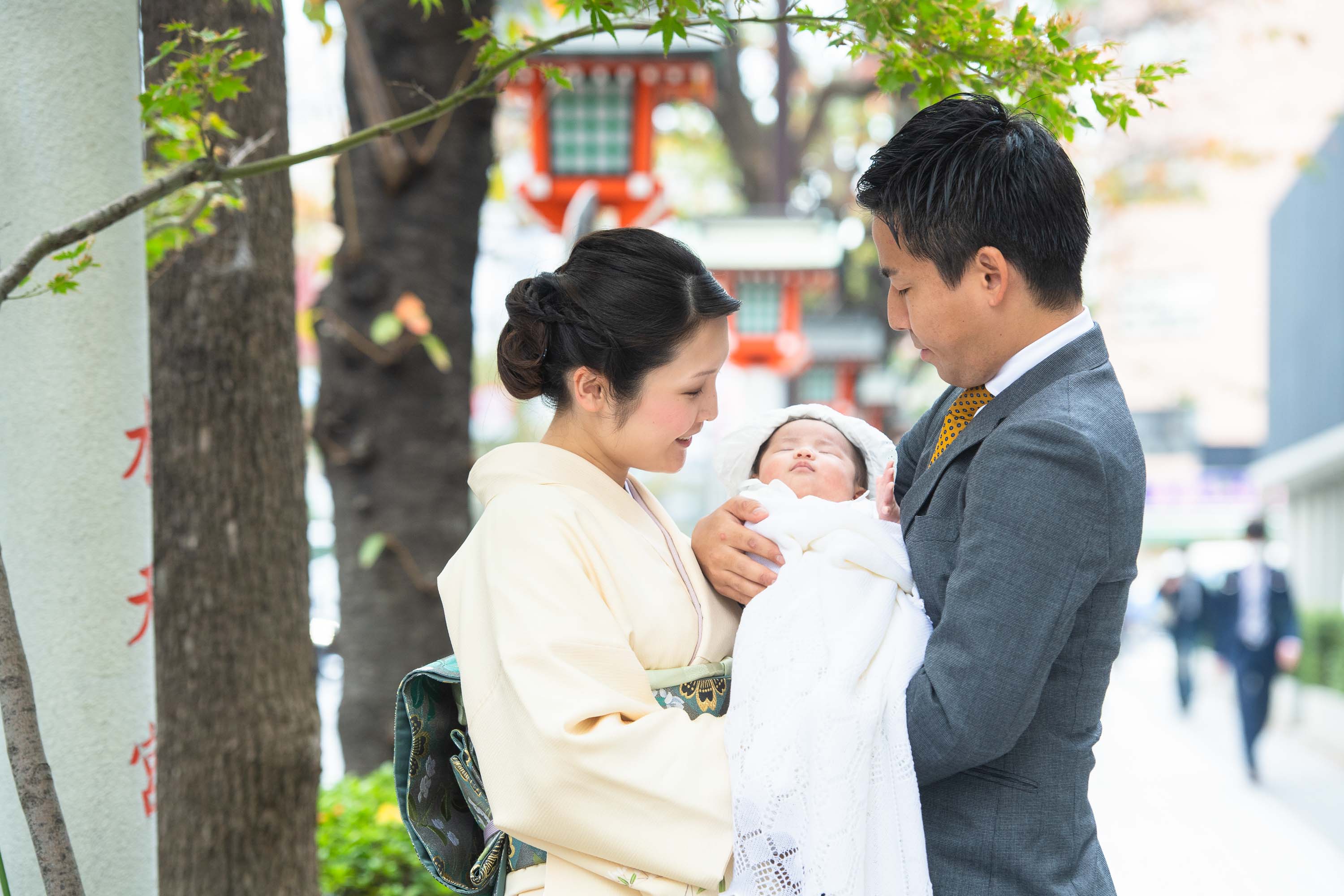 掛着を着た和装の女性に抱かれる赤ちゃんと横にいるスーツ姿の男性