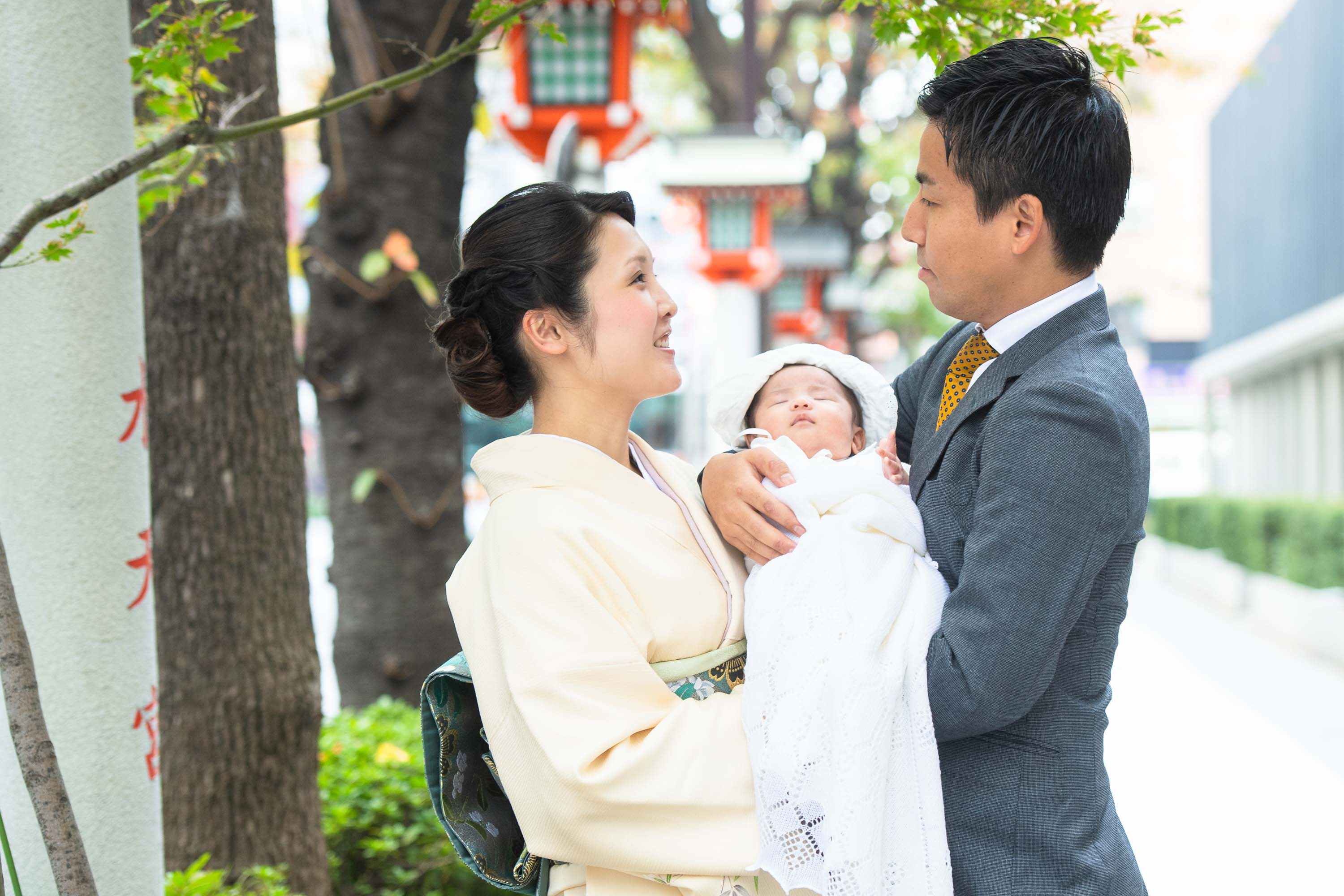 掛着を着た和装の女性に抱かれる赤ちゃんと横にいるスーツ姿の男性