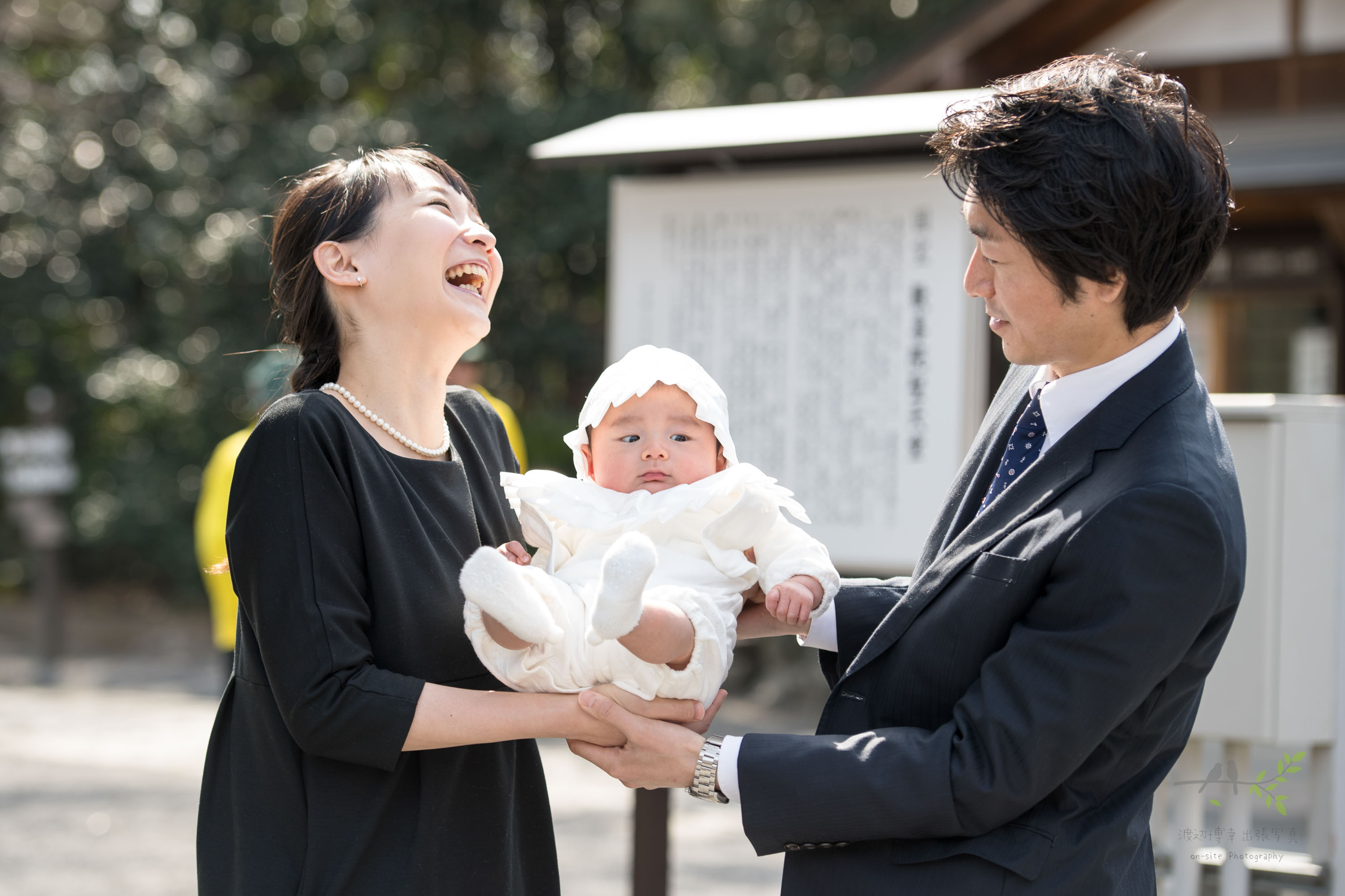 ベビードレスを着た赤ちゃんを両手で持ち上げる笑顔の女性と男性