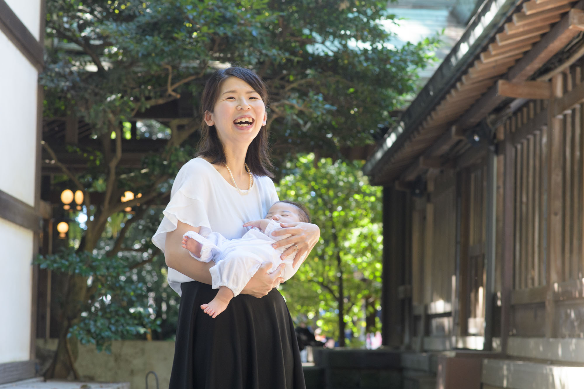 川越氷川神社でお宮参り白いワンピースで赤ちゃんを抱っこして笑うお宮参りの女性