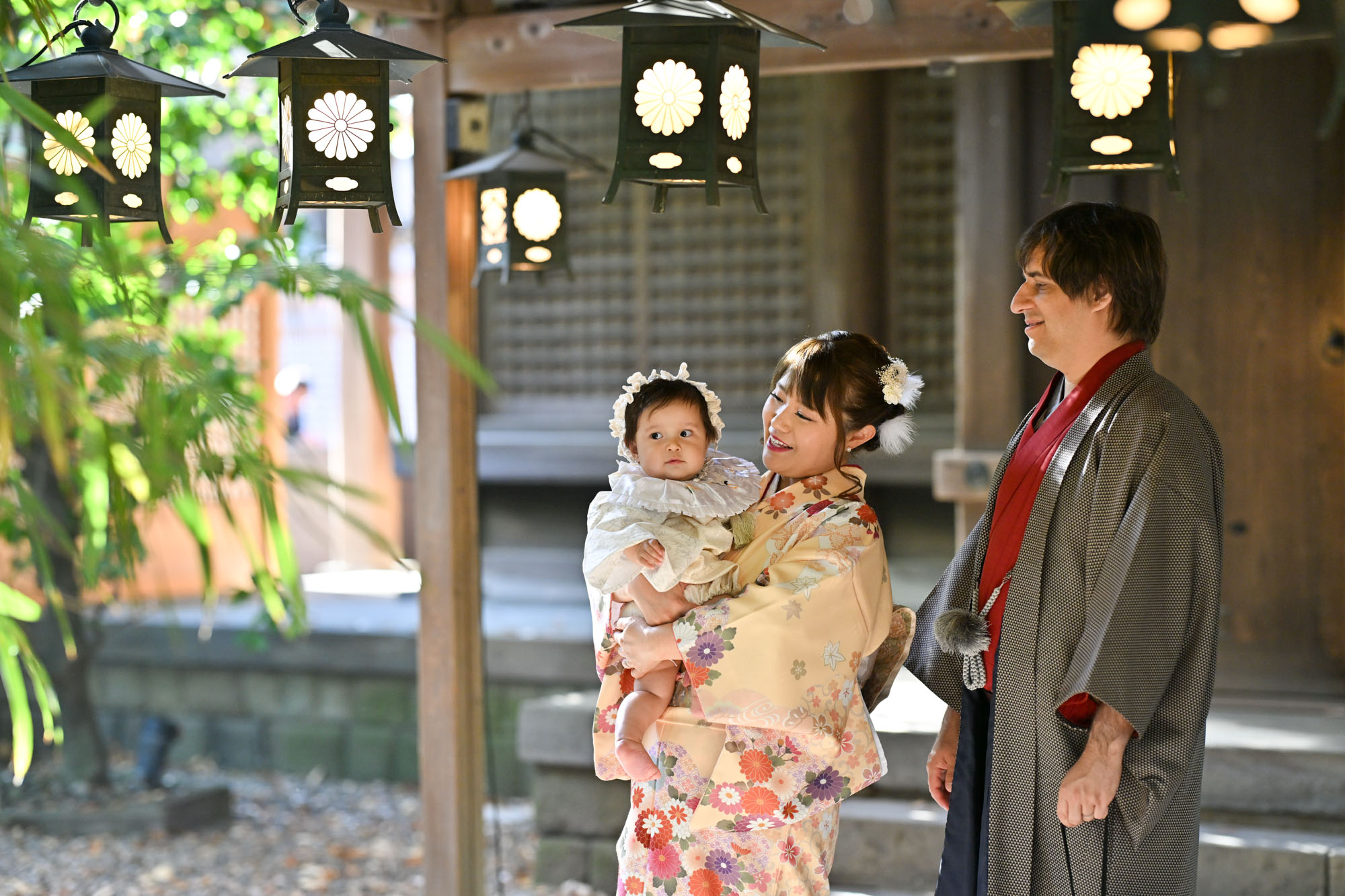川越氷川神社の回廊屋根の下で、赤ちゃんを泣く。着物姿のお宮参りの女性と横に立つ外国籍のパパ。