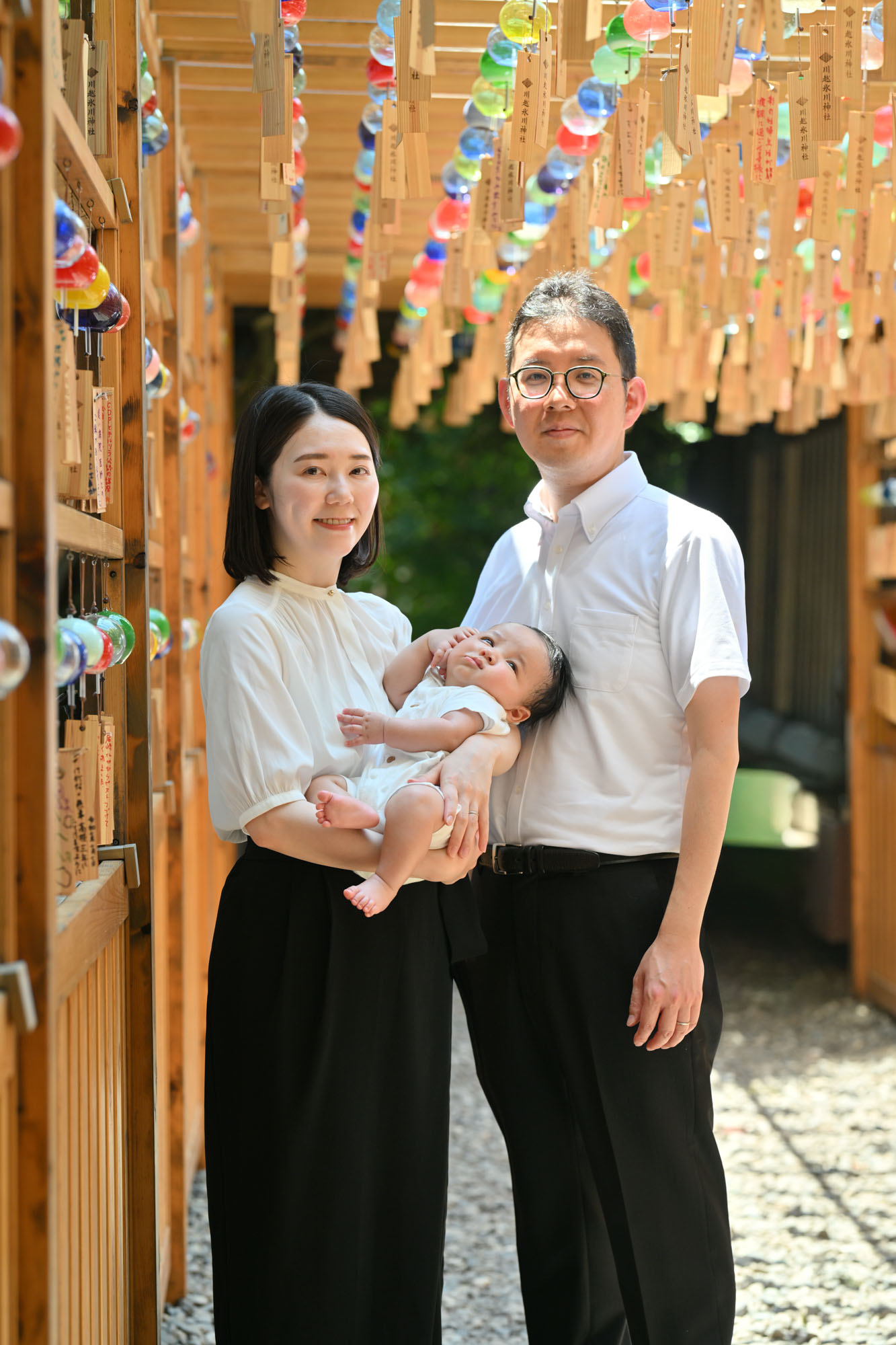 川越氷川神社縁結び風鈴の下で赤ちゃんを抱くお宮参りのママと横に立つパパ