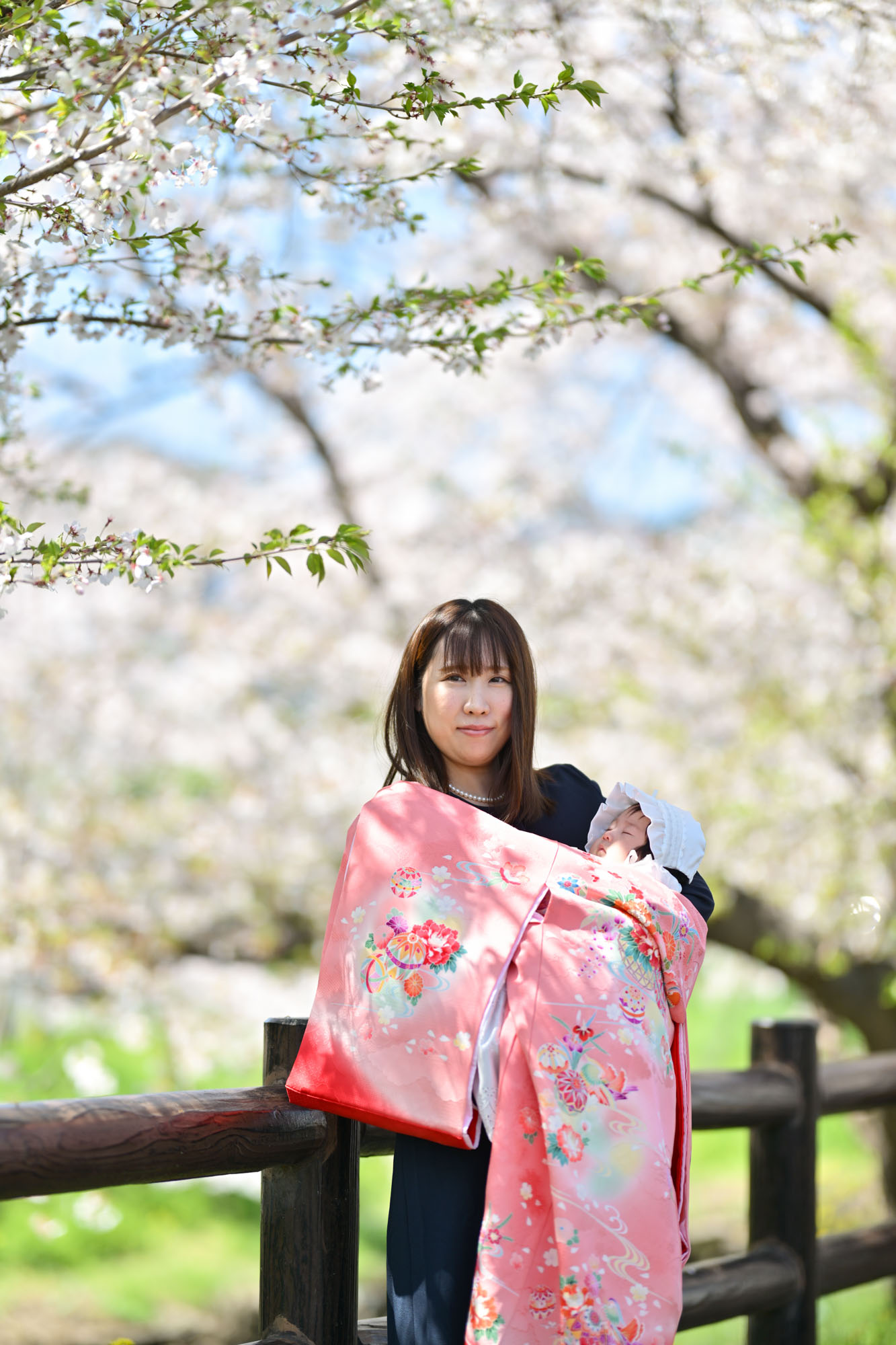 川越氷川神社の裏の新河岸側の桜バックのピンクの掛け着のお宮参りの女性