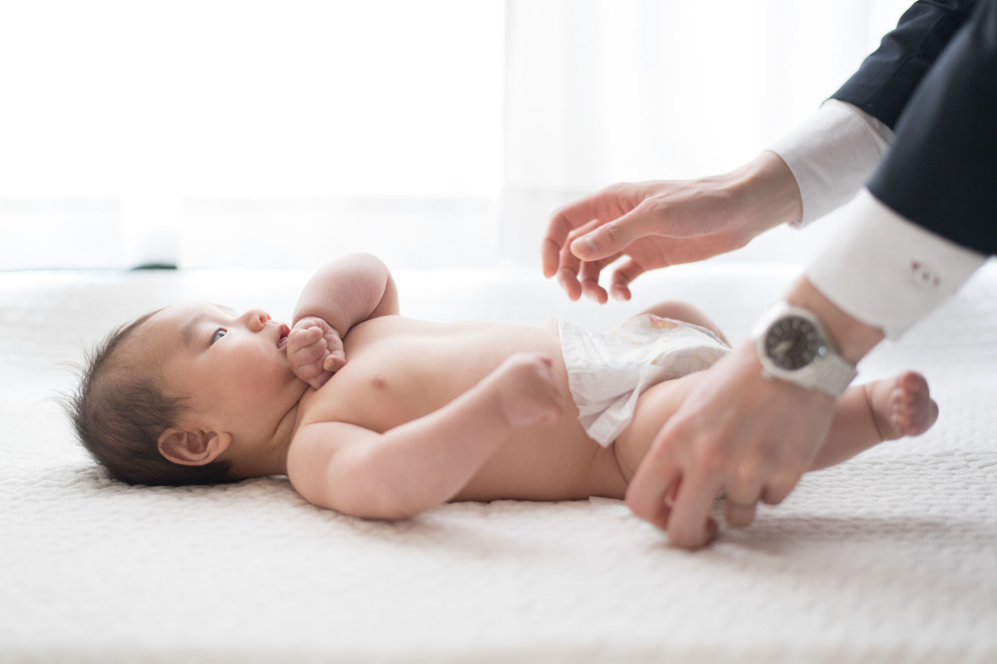 床に寝た赤ちゃんがオムツ替えをされている