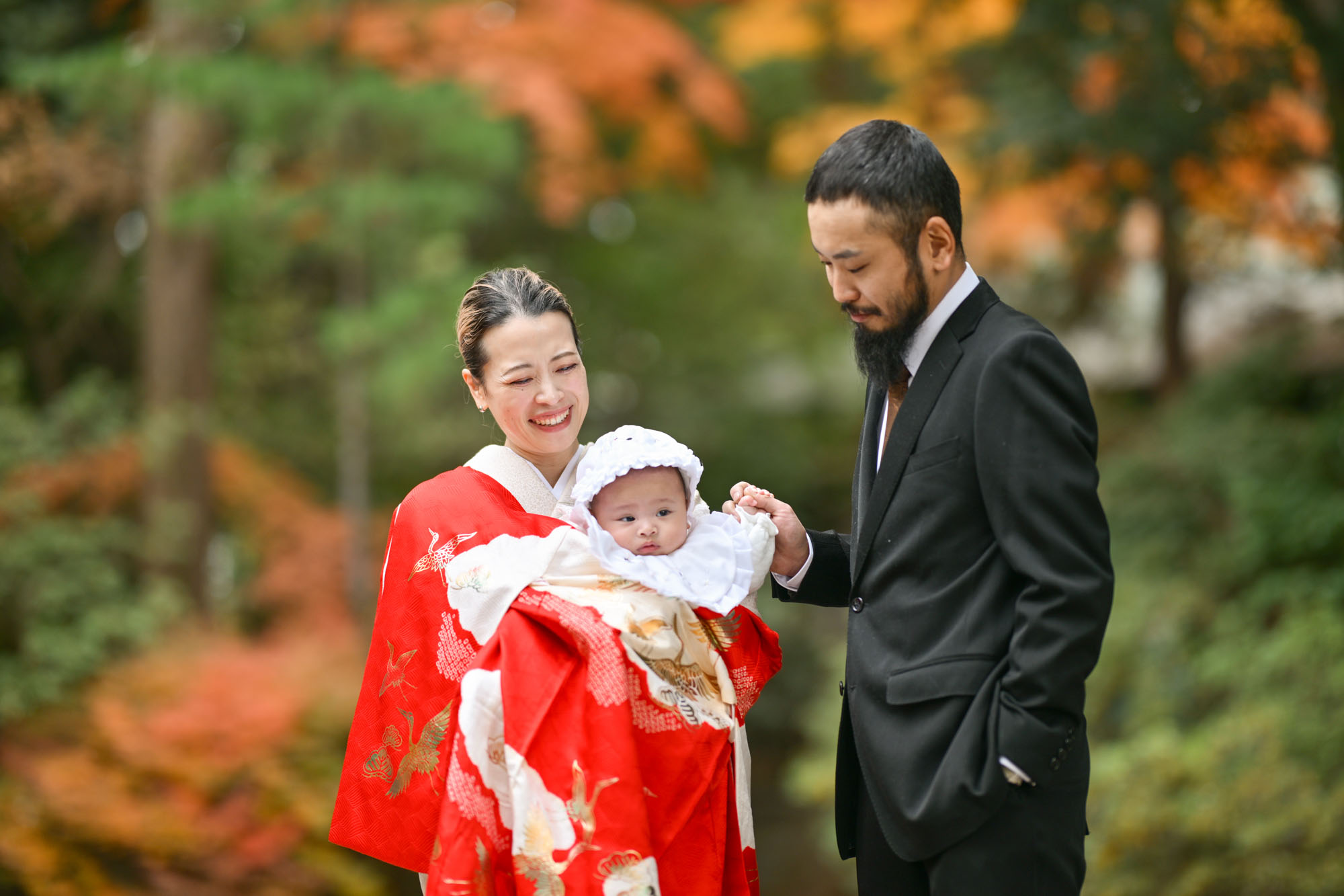 紅葉の中で赤ちゃんを抱っこする大宮氷川神社のお宮参りの夫婦