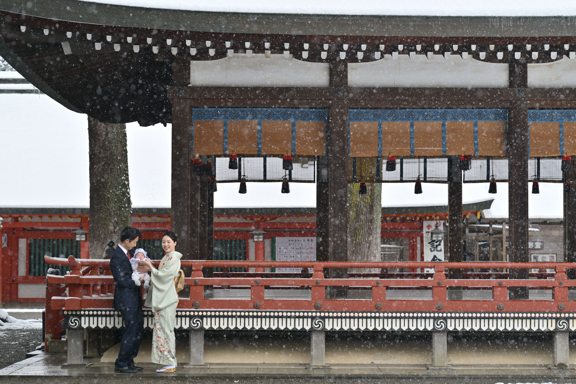 画像 大宮氷川神社のお宮参り雪の中の舞殿横で赤ちゃんを抱っこする御夫婦