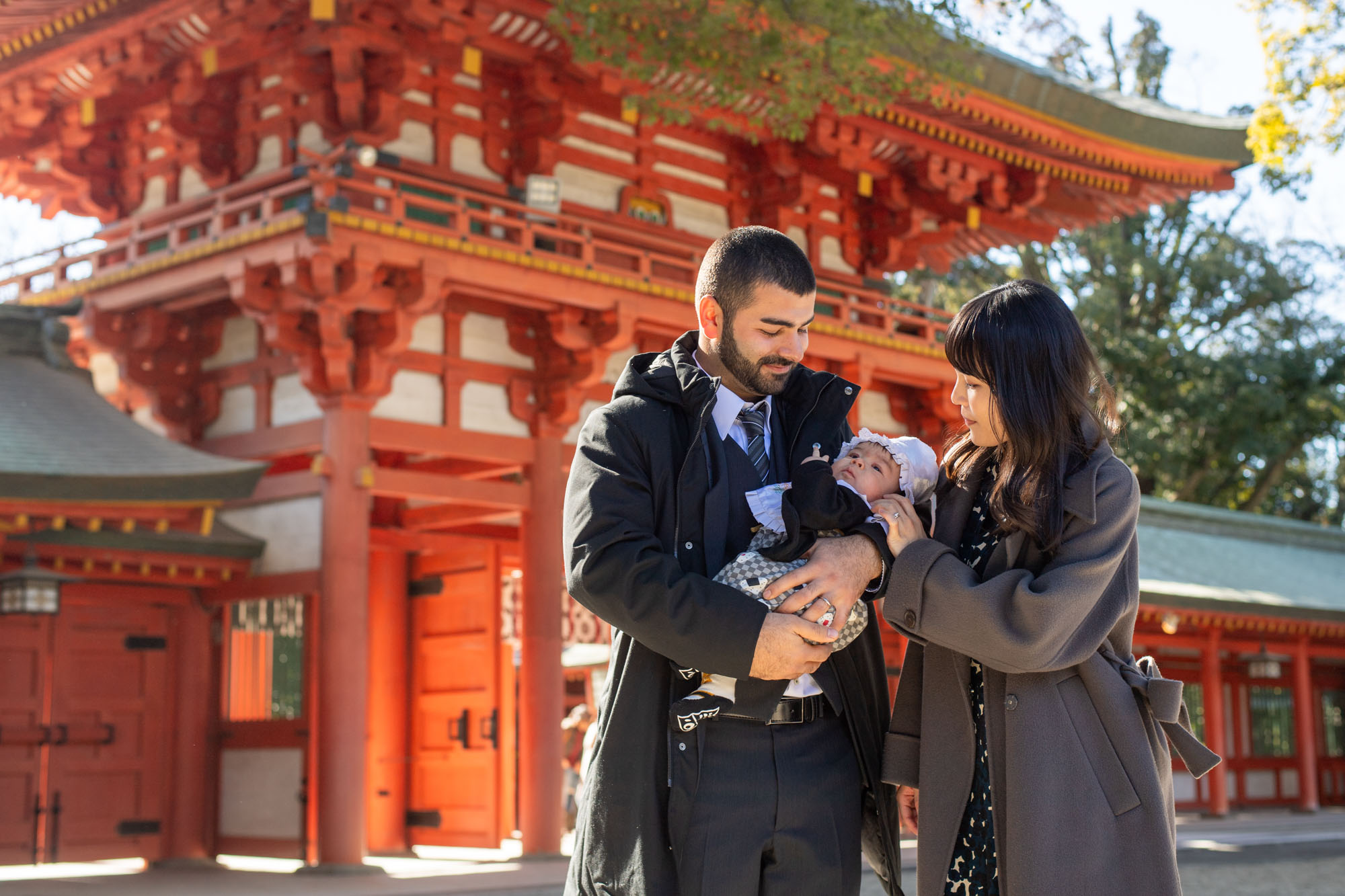 画像 大宮氷川神社のお宮参り、楼門をバックに赤ちゃんを抱っこしながら見つめるご夫婦