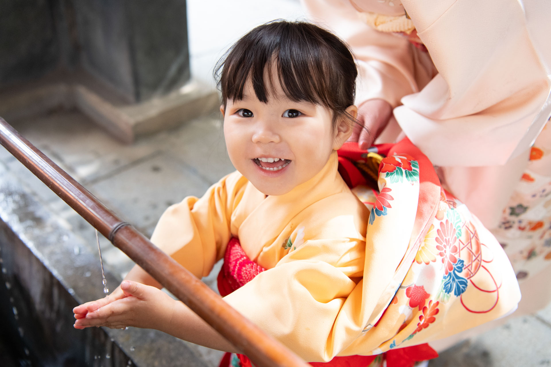 大宮氷川神社の手水舎で手を清める黄色い着物の女の子の七五三写真