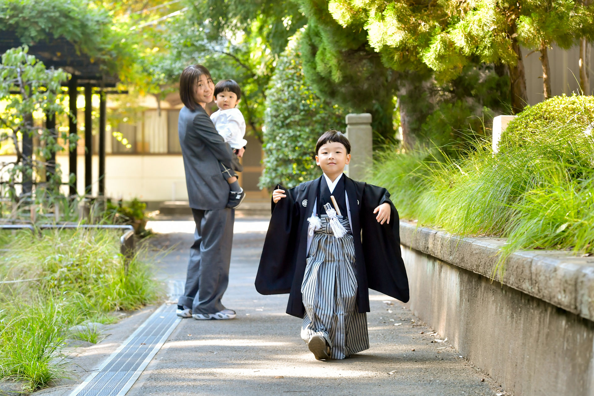 和楽備神社の参道・神社脇の道・植栽を歩く黒い着物を着た5歳の七五三の男の子